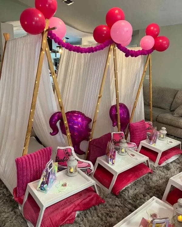 Indoor party setup with a Barbie theme, featuring small pink couches, tables, a balloon arch, and a draped tent for kids parties.