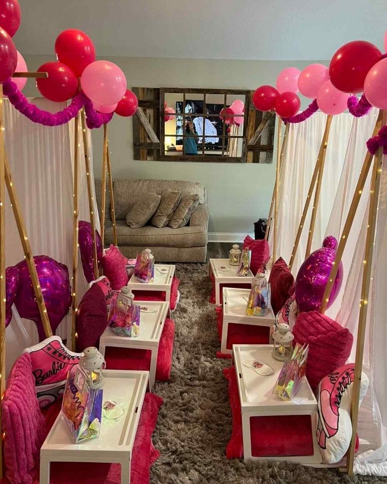 A pink and white party room transformed into a glamping paradise, complete with balloons, tables, and teepees for an unforgettable party experience.