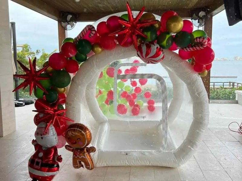 Inflatable snow globe decorated with red and gold balloons and stars, featuring a gingerbread man and Santa figure at a seaside pavilion, transformed into a winter wonderland.