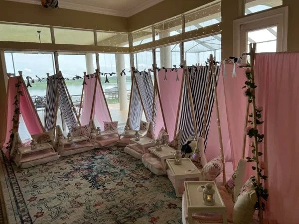 Interior of a sunroom with draped pink and striped canopies over individual pedicure stations, decorated with flowers, and an ocean view, designed to reflect a Night In Paris Theme event.