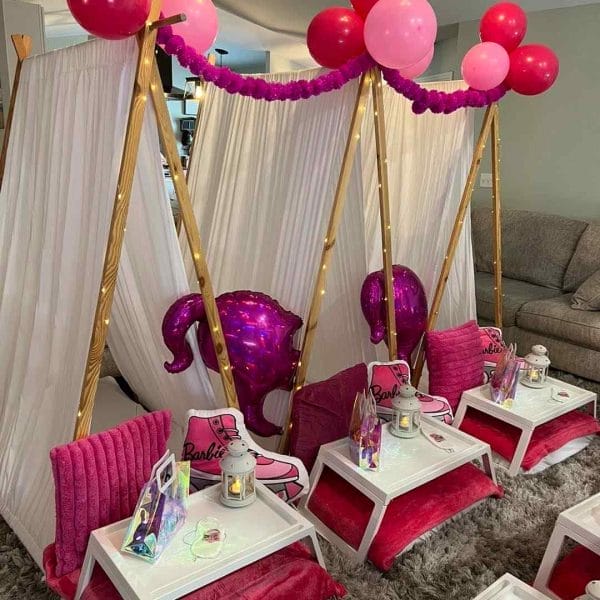 Indoor children's party setup featuring an ultimate sleepover upgrade with a Barbie theme, pink tents, balloons, and themed accessories.