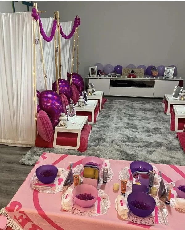 A Barbie Themed Party setup with pink and purple decorations, plush seating, and beauty treatment stations in a cozy room.
