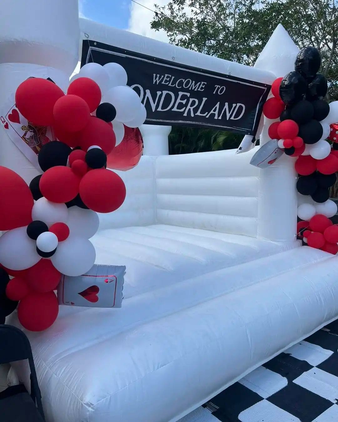 Inflatable entrance designed with a "welcome to wonderland" banner, decorated with red, black, and white balloons, featuring playing card elements.