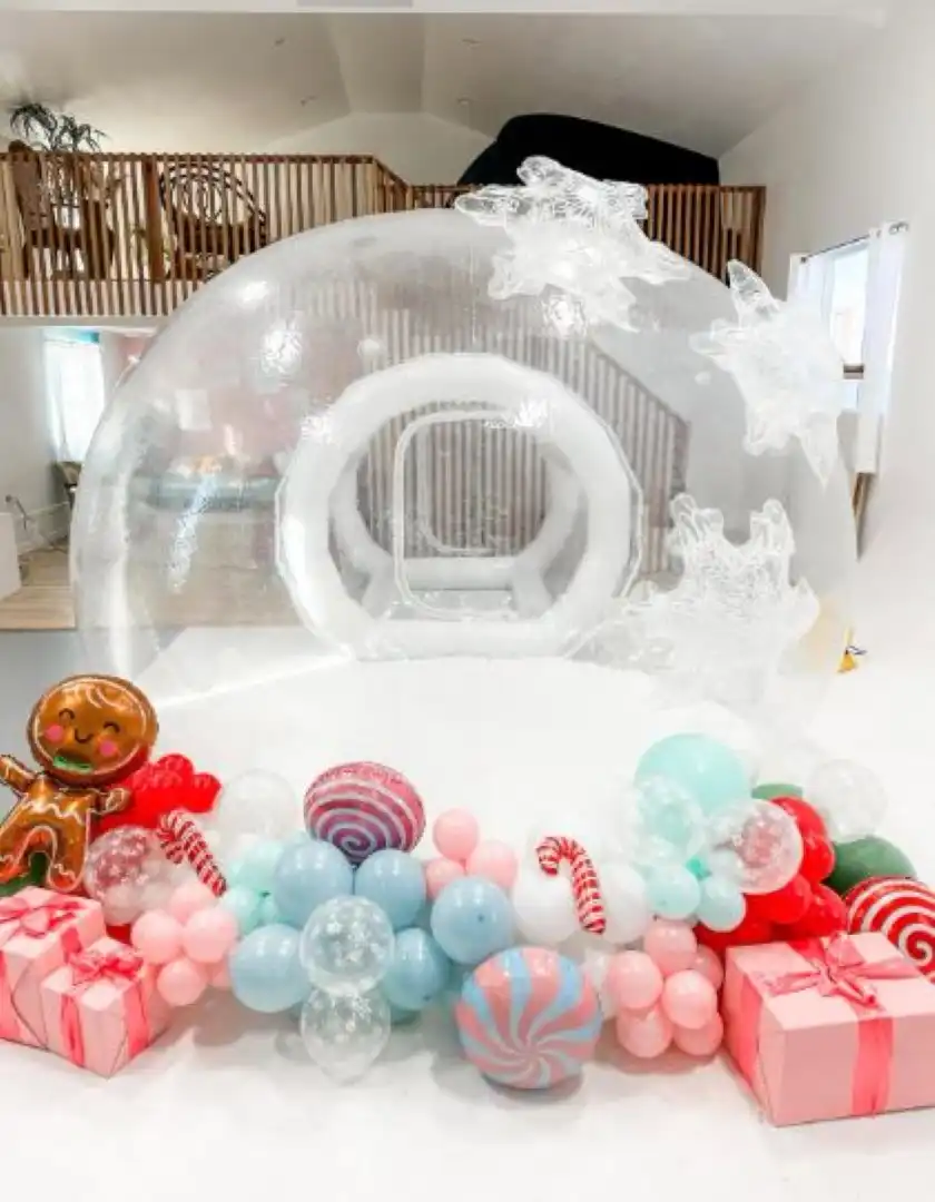 Inflatable snow globe with festive balloons and presents arranged in front of a white interior background.