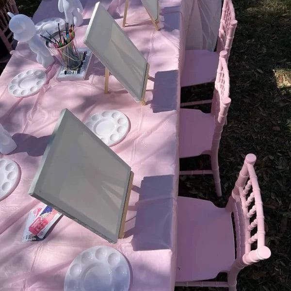 Outdoor Painting Party station with easels, chairs, and art supplies on pink tablecloths.