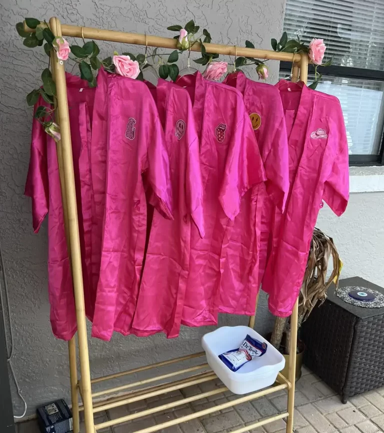 Pink choir robes hanging on a gold rack decorated with roses, with a white tub and a packet beneath it on a tiled patio set for a Spa Party with DIY lip Gloss.