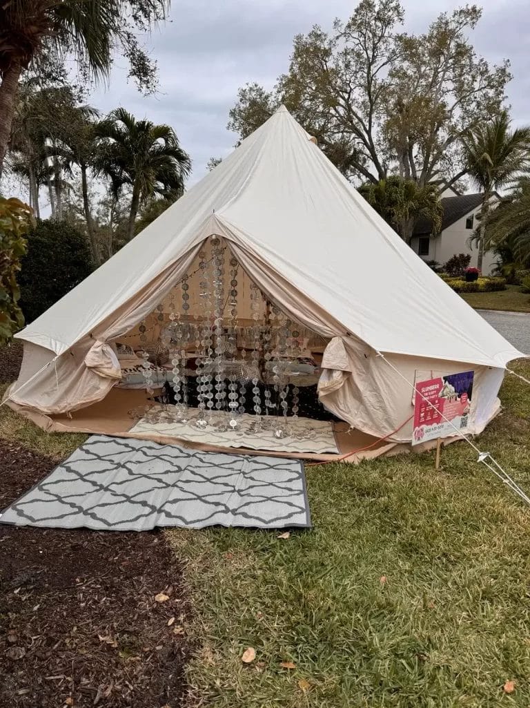 Sentence with Product Name: A large, ornate tent with an open flap revealing a decorated interior with lights and cushions for a Dream Catcher Themed Party, set up in a residential yard.