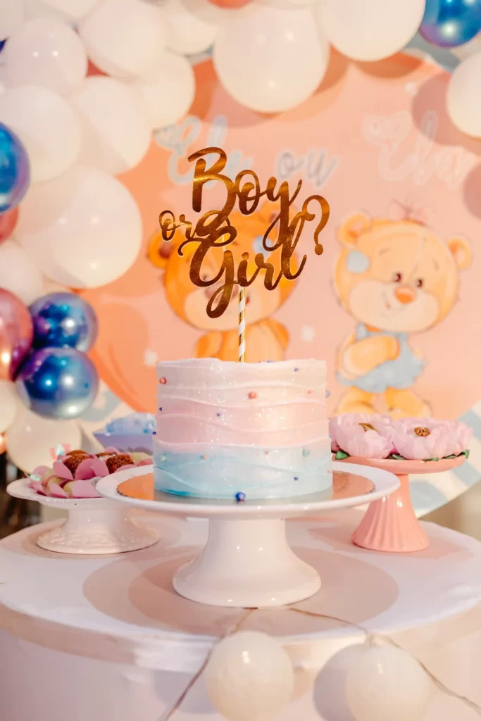 A Crafty Onesie Painting Party for Your Baby Shower with "boy or girl?" topper surrounded by balloons and a teddy bear decoration, set against a pastel-colored backdrop.